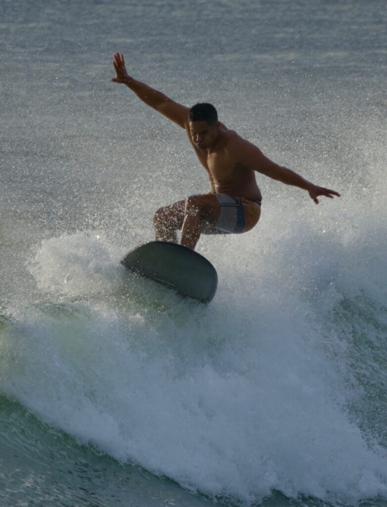 Surfer executing a dynamic maneuver on a wave, showcasing skill and balance amidst splashing water. Ideal for content on water sports.