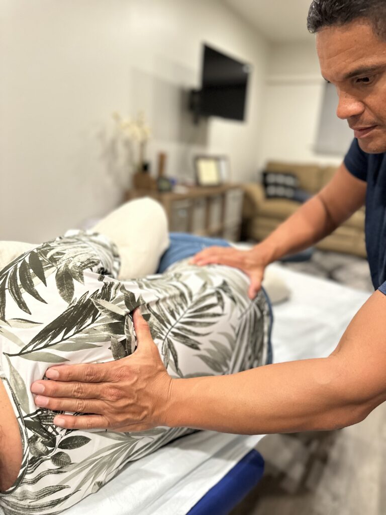 A therapist applies a manual technique to a client's back during a treatment session in a calming, well-lit space.
