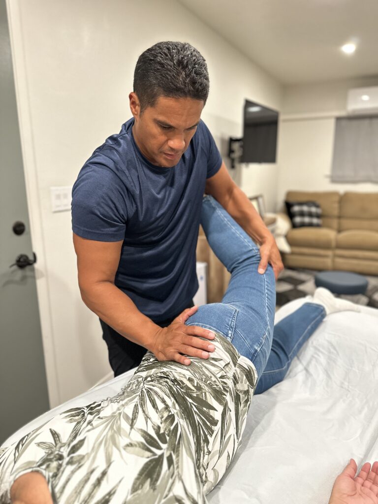 A therapist performs leg manipulation on a patient in a home setting, focusing on physical therapy or rehabilitation techniques.